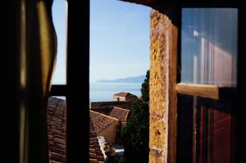 Charming Mediterranean coastal view through a rustic window with terracotta rooftops and sea horizon.