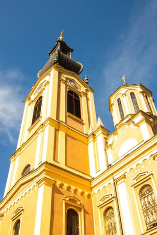 A bright yellow church with intricate architecture and a clear blue sky in Bosnia and Herzegovina.