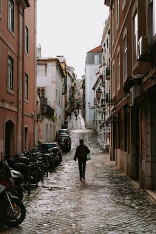 A person walks down a cobblestone street in the historic district of Lisbon, Portugal.