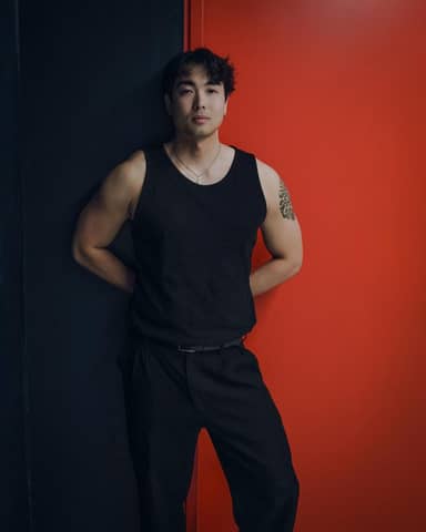 Portrait of a stylish man in black attire leaning against a vivid red wall.