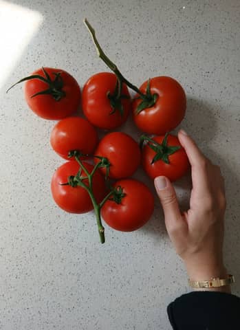Hand touching fresh red tomatoes on a speckled kitchen counter.