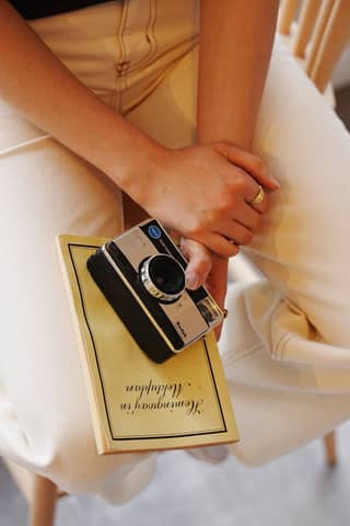 Close-up of hands holding a vintage camera and book indoors, evoking nostalgia.