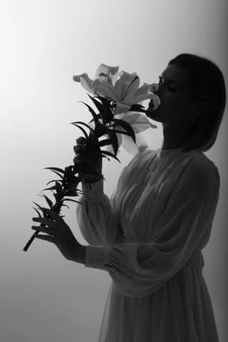 Elegant black and white portrait featuring a woman holding and smelling a lily flower in a studio setting.