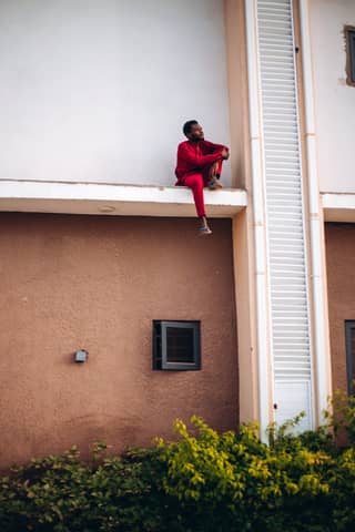 Man in red outfit sitting on building ledge, showcasing urban adventure and boldness.