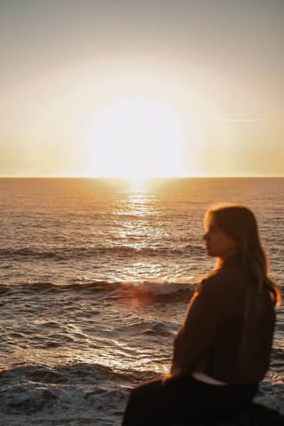 Silhouette of a person sitting by the ocean during a vibrant sunset.