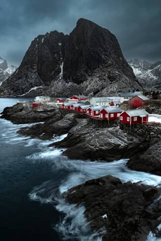 Dramatic coastal view of red huts in Nordland, Norway under moody skies.