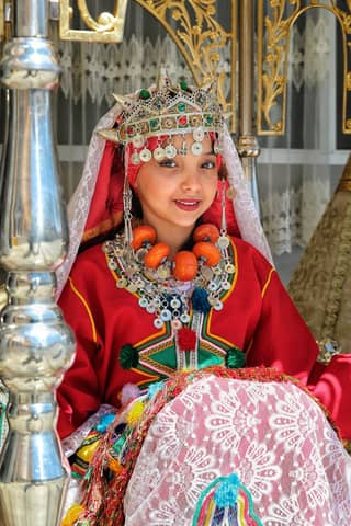 Colorful traditional attire with intricate jewelry and headdress in a cultural setting.