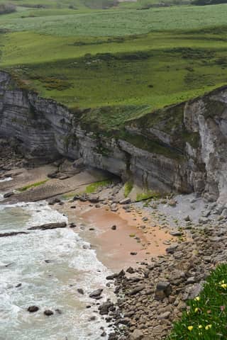Dramatic coastal cliffs and beach in Tagle, Spain with lush greenery.