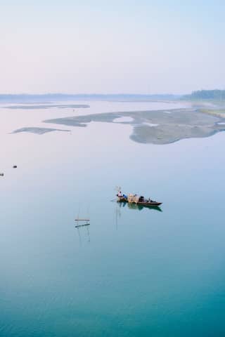 A tranquil scene of a boat on a calm river in Kurigram, Bangladesh, under a clear blue sky.