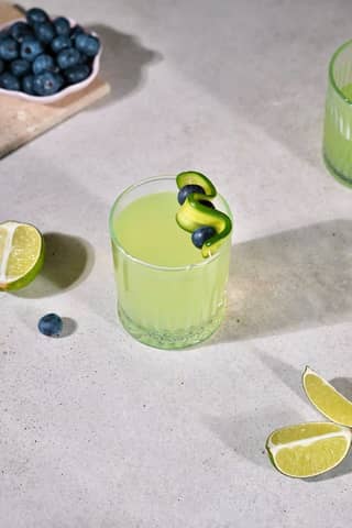 Lime juice with cucumber and blueberry garnish on a concrete surface, ideal for summer refreshment.