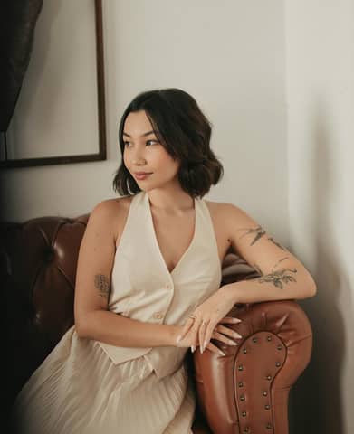 Elegant woman with tattoos relaxing indoors on a leather sofa. Modern and stylish interior.