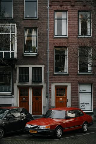 Vintage red car parked in front of historic Amsterdam canal houses.