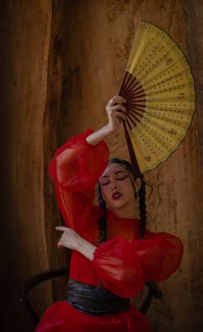 Artistic portrait of a woman in red dress holding a fan, showcasing elegance and cultural expression.
